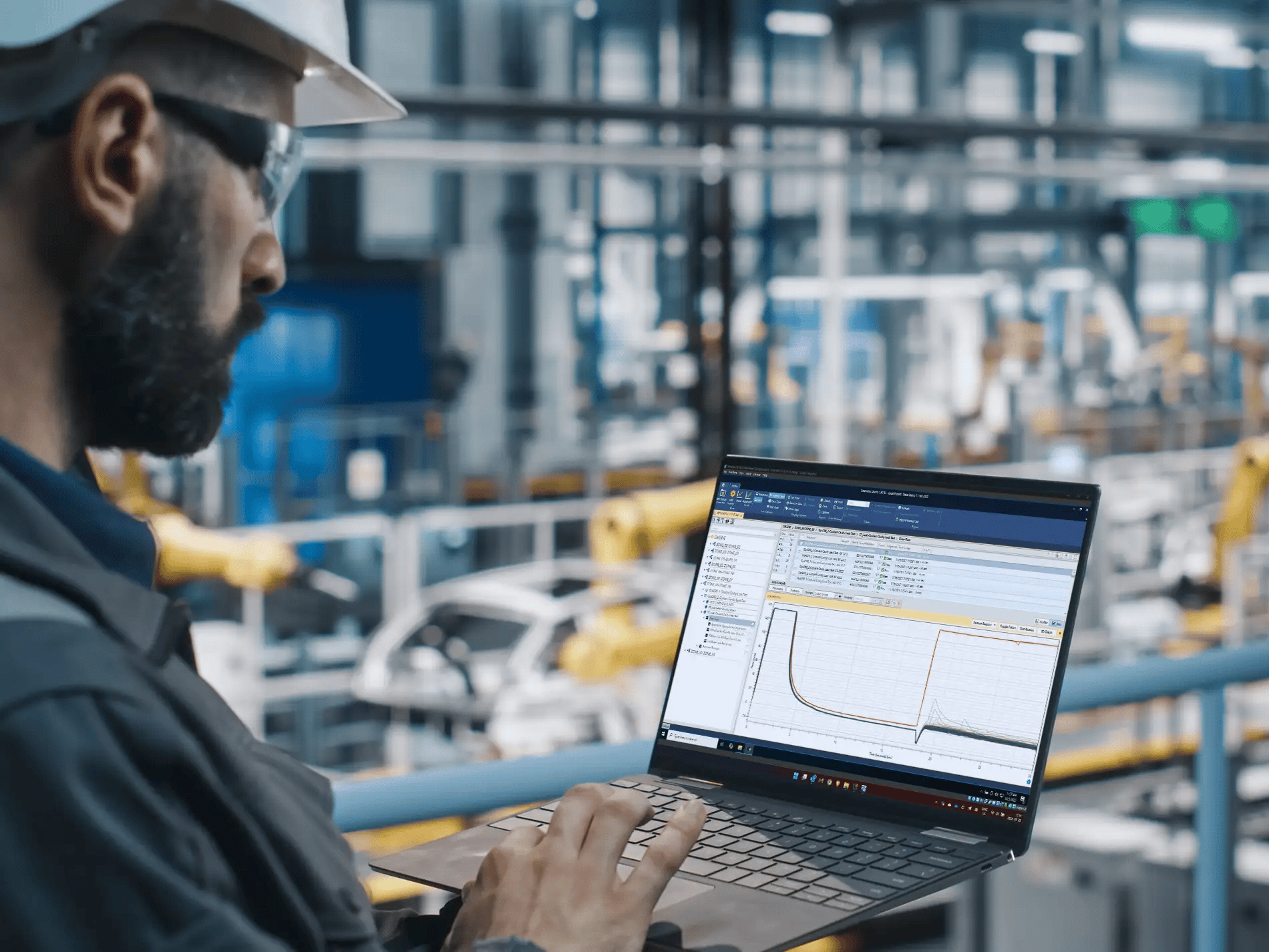 A man with a beard and hard hat looking at graphs on the computer.