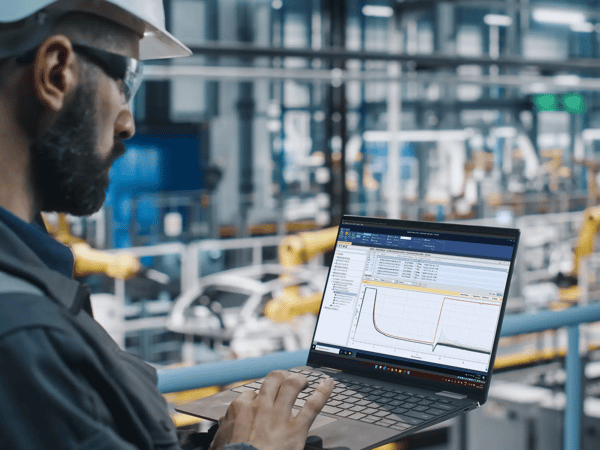 A man with a beard and hard hat looking at graphs on the computer.