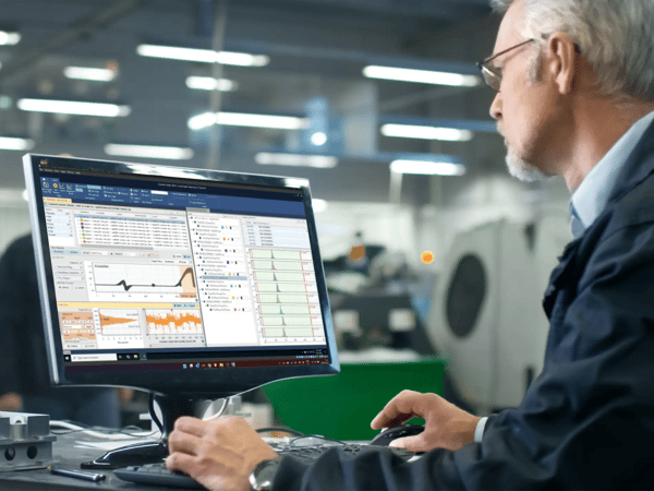 Older man on the right sitting at a desk in a manufacturing environment looking at a computer monitor with Sciemetric Studio data