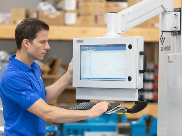 Man looking at a Dynics monitor attached to a machine with a flexible arm, with one hand on the keyboard.