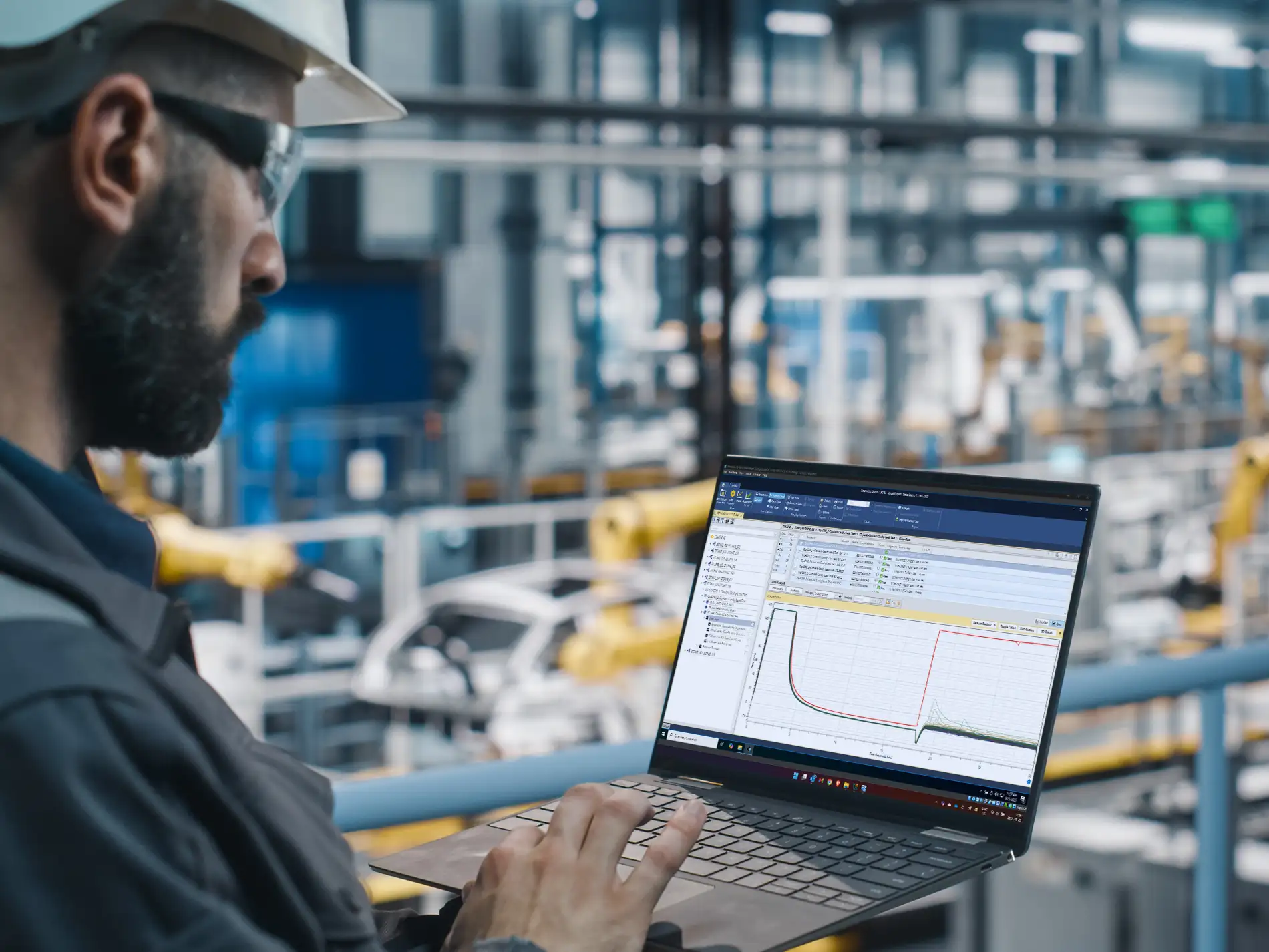 A man with a beard and hard hat looking at graphs on the computer.
